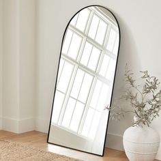 a mirror sitting on top of a wooden floor next to a vase