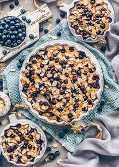 two pies with blueberries and other toppings sitting on top of a table