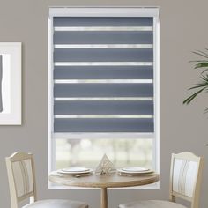 a dining room table with two chairs and a large window covered in roman blind shades