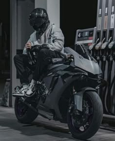 a man sitting on top of a motorcycle next to a gas station pump and filling it with fuel