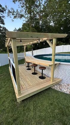 a wooden gazebo sitting on top of a lush green field next to a swimming pool