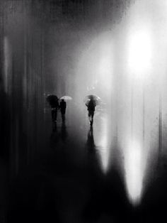 three people with umbrellas walking in the rain on a dark street under bright lights