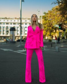 a woman standing in the middle of a street wearing bright pink pants and a blazer