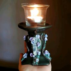 a hand holding a glass candle holder with flowers on it and a lit candle in the middle