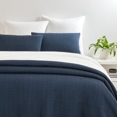 a bed with blue and white comforters in a bedroom next to a plant on a nightstand