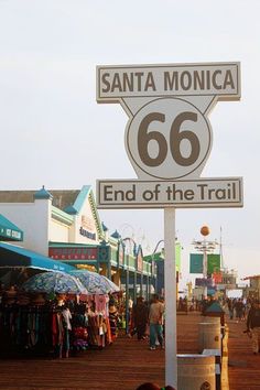 a street sign that says santa monica 66 end of the trail with people walking around