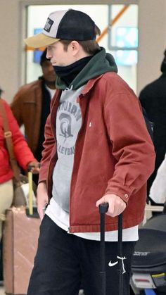 a man in a red jacket and black hat pulling luggage behind him at an airport