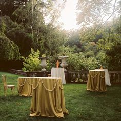 an outdoor setting with tables and chairs covered in gold cloths, surrounded by greenery