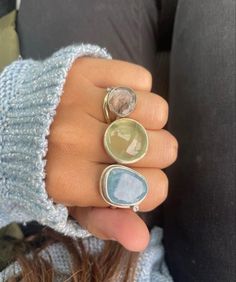 Picture of a girls hand wearing 3 large trendy gemstone rings on 3 fingers wearing a blue long sleeve shirt. Rings in order from top to bottom are rutile quartz (clear transparent ring with little strings inside), prehnite (transparent green), and aquamarine (transparent light blue) with silver bands Mode Inspo, Mode Inspiration