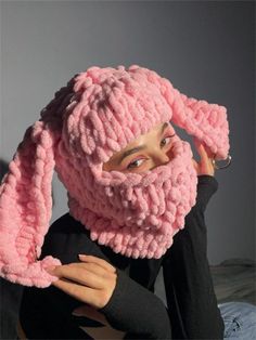 a woman wearing a pink knitted bunny hat and scarf with her hands on her head