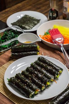 there are several plates with sushi on the table next to bowls of veggies