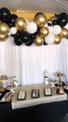 a table topped with lots of black and white balloons next to a wall filled with gold and white desserts