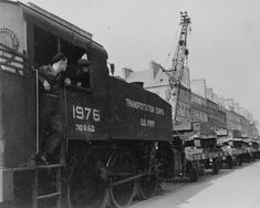 an old black and white photo of men on the side of a train car with other cars in the background