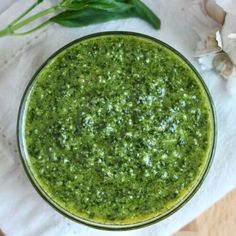 a glass bowl filled with green pesto on top of a white napkin next to garlic