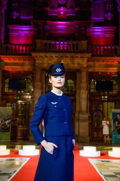 a woman in an air force uniform standing on a red carpet with purple lights behind her