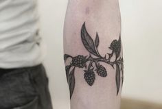 a person with a tattoo on their arm is standing next to a white wall and there are black berries