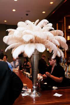 a tall vase filled with white feathers sitting on top of a wooden table next to a bar