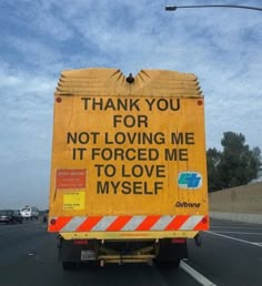 a yellow truck driving down a road with a thank you sign on it's back