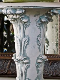 an ornate white pedestal with a mirror in the back ground and a vase on top