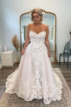 a woman standing in front of a mirror wearing a wedding dress with white flowers on it