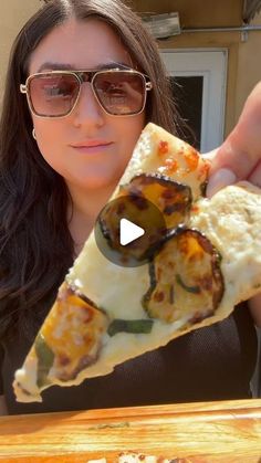 a woman holding up a slice of pizza in front of her face and wearing sunglasses