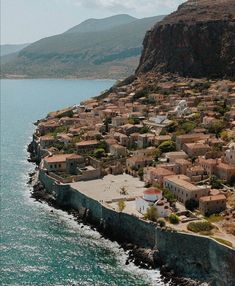 an aerial view of a small village by the ocean with mountains in the background and blue water