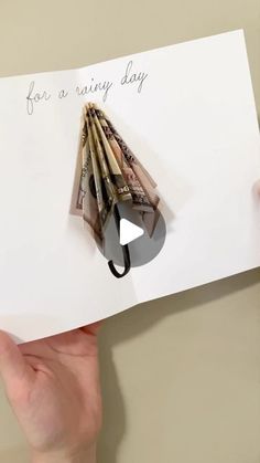 someone holding up a piece of paper with money folded into the shape of an umbrella