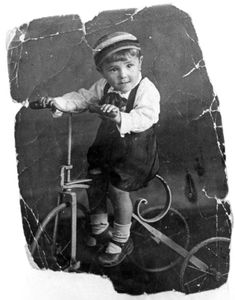 an old black and white photo of a young boy on a bike with a hat