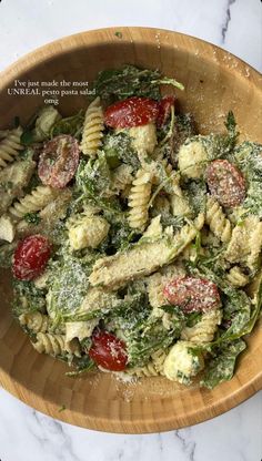 a wooden bowl filled with pasta covered in pesto and tomato sauce on top of a marble counter