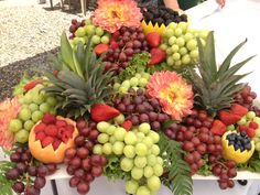 a table topped with lots of fruit and flowers next to a white plate filled with grapes