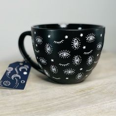 a black coffee cup with white designs on it and a blue tag next to it