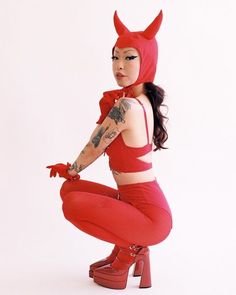 a woman in red is kneeling down with her legs crossed and wearing devil horns on her head