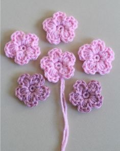 four crocheted flowers on a white surface with a pink string in the middle