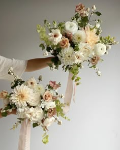 two bridal bouquets being held up by someone's hands with flowers on them