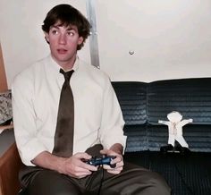 a man sitting on a couch holding a video game controller in his hand and looking at the camera