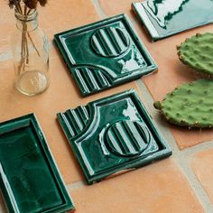 three green plates sitting on top of a tiled floor next to a vase with flowers