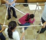 several children are playing with an object made out of sticks and tape on the floor