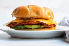 a bacon, egg and avocado sandwich on a white plate next to a napkin