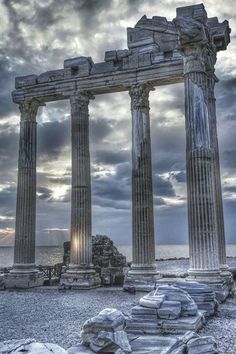 black and white photograph of ancient ruins on the beach with sun shining through clouds above