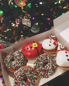 a box filled with donuts covered in frosting and sprinkles next to a christmas tree