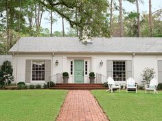 a white house with two lawn chairs in front of it and a green door on the side