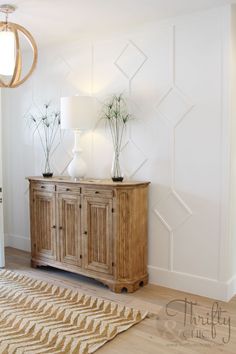 a wooden cabinet sitting next to a lamp on top of a hard wood floor in front of a white wall