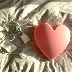 a pink heart shaped object laying on top of a bed next to a charger