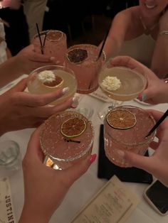 four people are holding up their glasses with drinks in them on a table at a party