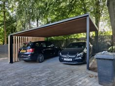 two cars are parked in a carport on the side of a brick road next to trees