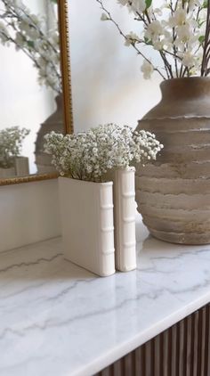 two vases with flowers are sitting on a marble countertop next to a mirror