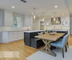 a large kitchen with white cabinets and wooden table in the center is surrounded by blue chairs