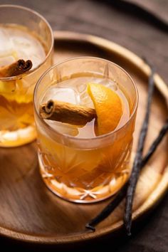 two glasses filled with drinks sitting on top of a wooden tray next to cinnamon sticks