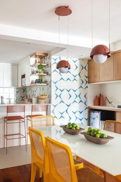 a white table with yellow chairs and bowls of fruit on it in a kitchen area