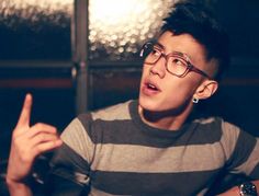 a young man wearing glasses sitting at a table with food in front of him and pointing to the side